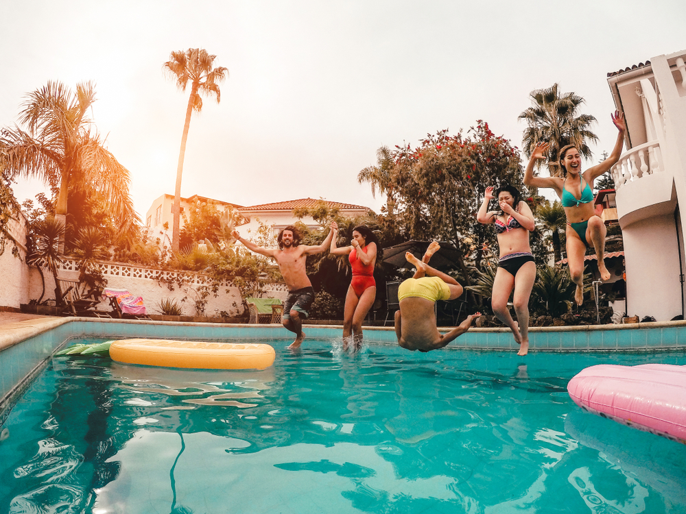 Group,Of,Happy,Friends,Jumping,In,Pool,At,Sunset,Time